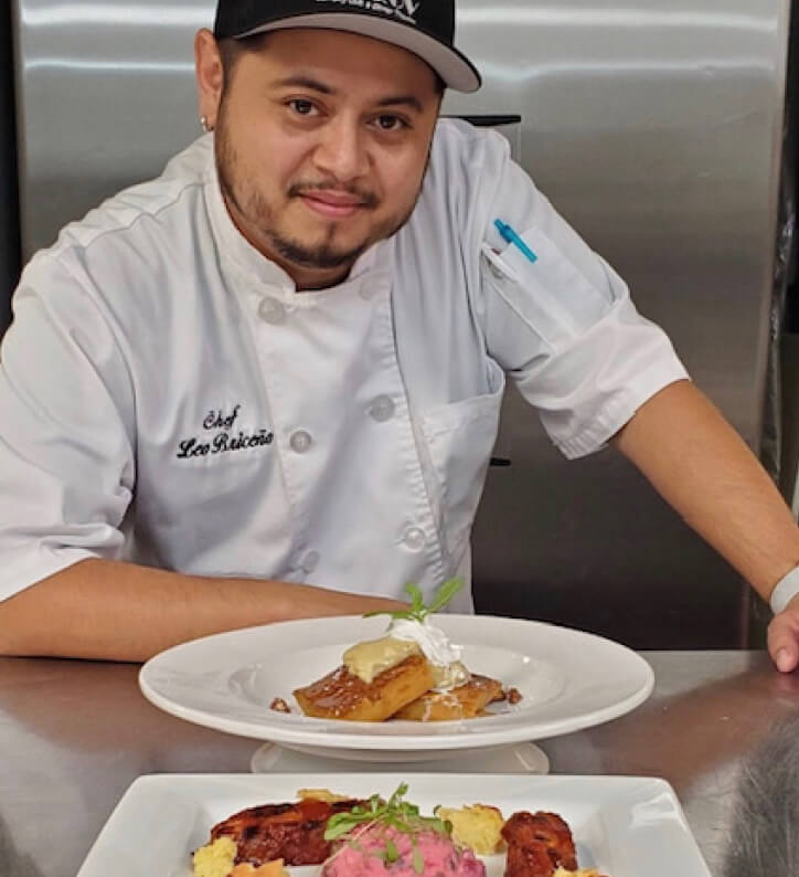 chef standing behind a plate of food smiling