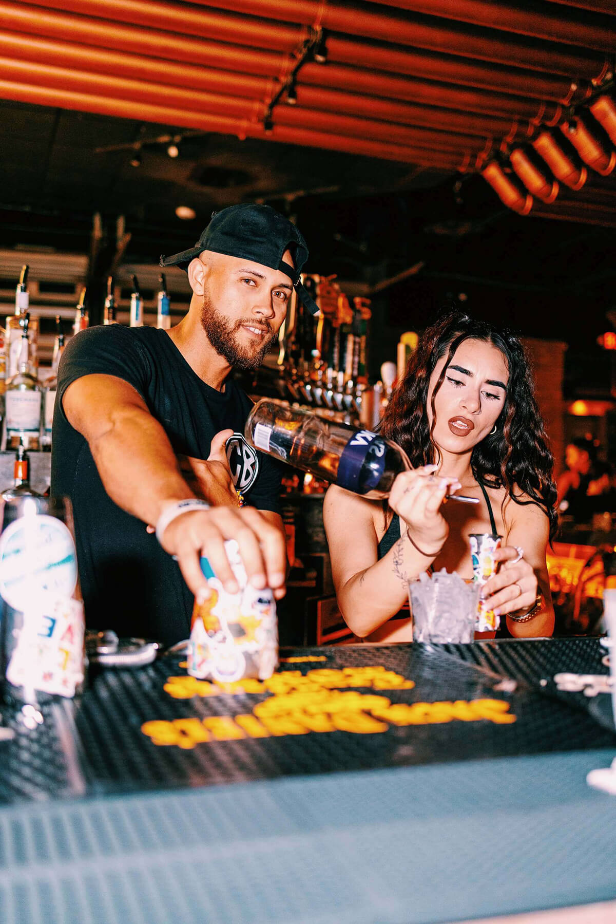 two bartenders pouring drinks at the bar smiling